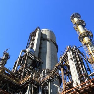 A towering industrial plant under a vivid blue sky, showcasing its intricate architecture and industrial prowess.